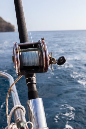 Close up of a heavy duty reel with the bright blue ocean in the background.