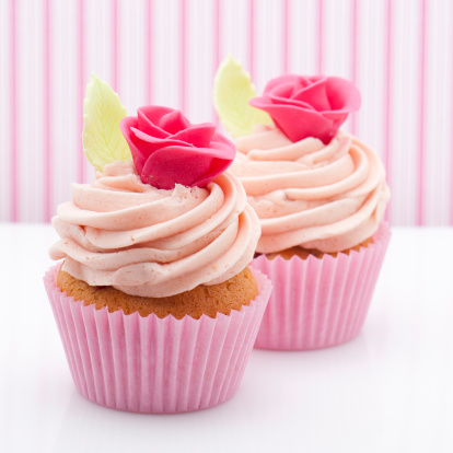 Pink cupcakes with rose decorations and pink, striped wallpaper in the background.