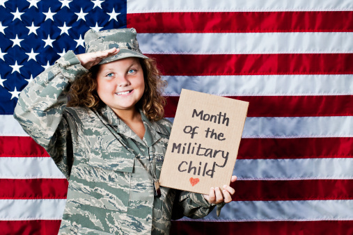 Ten year old little girl in military uniform holding sign for Month of the Military Child and saluting