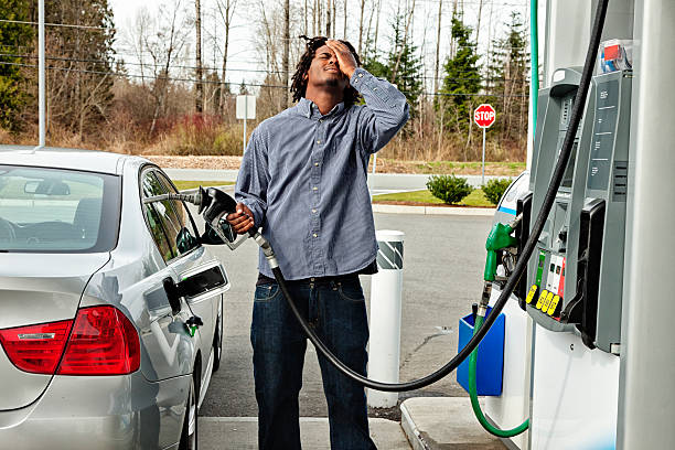 Gas Station Frustration Photo of a young man agonizing over how much it costs to fill his gas tank. fuel prices photos stock pictures, royalty-free photos & images