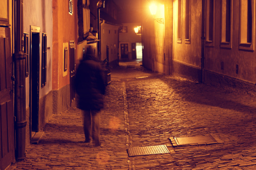 Unrecognizable motion blurred person in the night. Location: the famous medieval street of Prague, the Golden lane at night. 