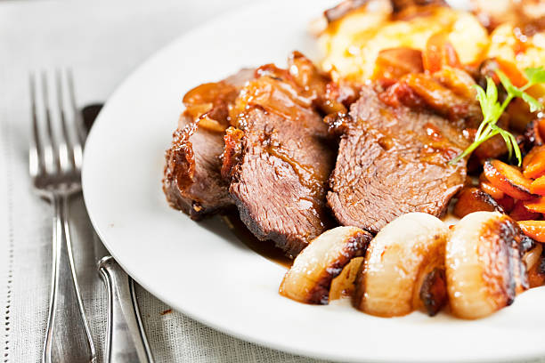 roast beef slices of roast beef on plate, surrounded by roast onoins and carrots german food photos stock pictures, royalty-free photos & images