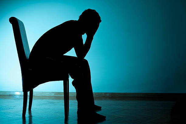 Depression Depressed young man sitting on chair with face in his hands silhouette of depressing stock pictures, royalty-free photos & images