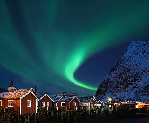 Northern lights - Aurora borealis over Reine, Lofoten, Norway Lovely shape of Northern lights (Aurora borealis) over traditional norwegian fishing lodges (rorbuer) and snowy mountain.  reine lofoten stock pictures, royalty-free photos & images
