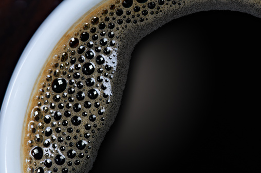 A closeup shot of a cup of black coffee with tiny bubbles 