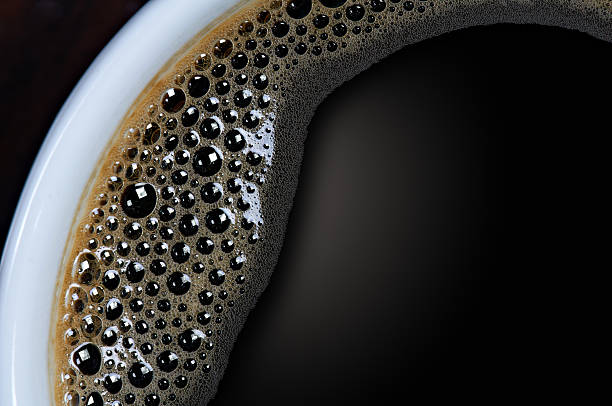 A closeup shot of a cup of black coffee with tiny bubbles  Top view of white cup with black coffee.  Close-up black coffee stock pictures, royalty-free photos & images