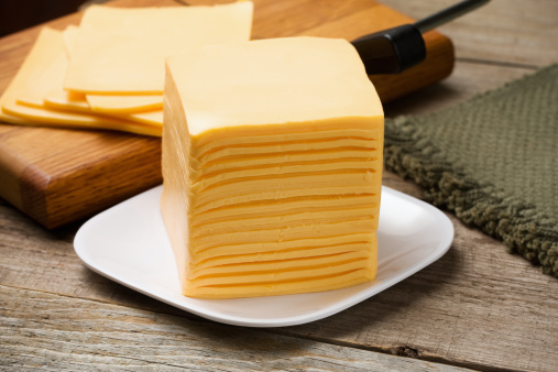 Stack of sliced cheese on a plate in front of a cheese slicer.