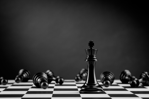 Leader and competition. Black Chess King on chessboard against lying chess pawns.