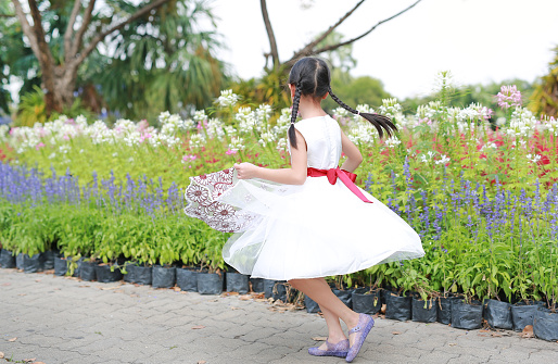 Asian little girl in white dress running and having fun in the flower garden.