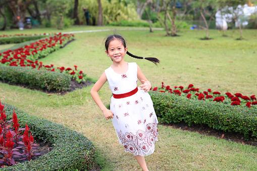 Happy Asian little girl in white dress running and having fun in the flower garden.