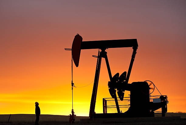 Pumpjack Silhouette With Worker A silhouette of a pumpjack on the prairie with maintenance worker standing by. Alberta, Canada. Oil and gas concept. oil pump oil industry alberta equipment stock pictures, royalty-free photos & images