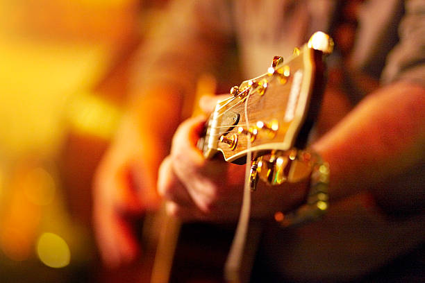 young man playing acoustic guitar in concert Part of a guitar player, available light , high iso shot, shallow depth of field! bunt stock pictures, royalty-free photos & images