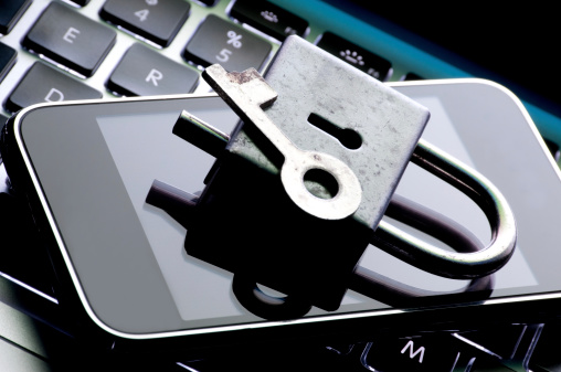 Old antique lock and key sitting on a cell phone on an illuminated keyboard.