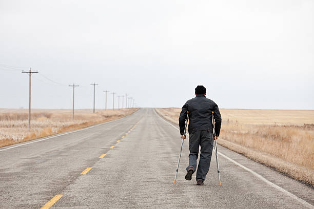 istock Injured Man Walking Down A Desolate Highway With Crutches 155375739
