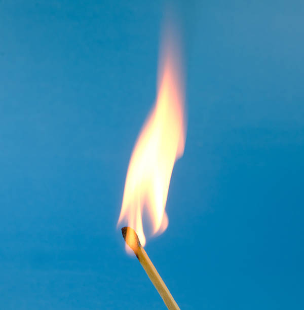 Flaming Match on Blue A yellow and orange  flame coming from an ignited wood match. Blue background ... Copy space on the flame. lit match stock pictures, royalty-free photos & images