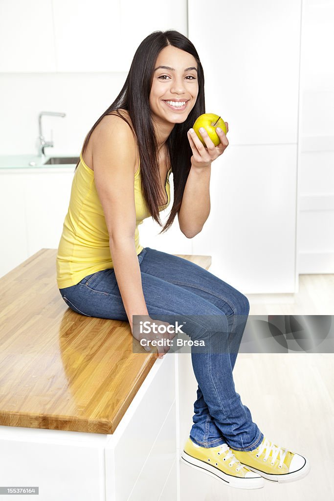 Joven mujer comiendo una manzana en una moderna cocina - Foto de stock de 20 a 29 años libre de derechos