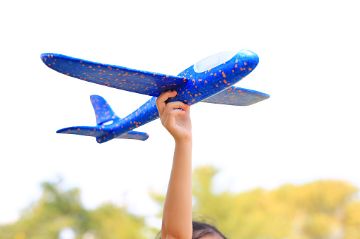 Closeup child hand raise up a blue toy airplane flying over white sky background in the garden.