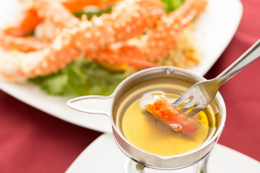 King Crab Dipped in Clarified Butter with a plate of crab blurred in the background