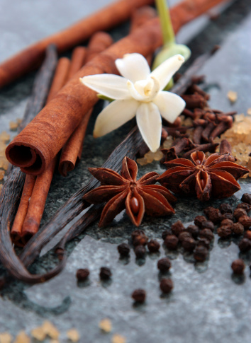 Raw spices of star anise, peppercorns, cinnamon, vanilla beans, and cloves arranged with sugar granules on a marble bench top.  Narrow DOF.  Focus on star anise