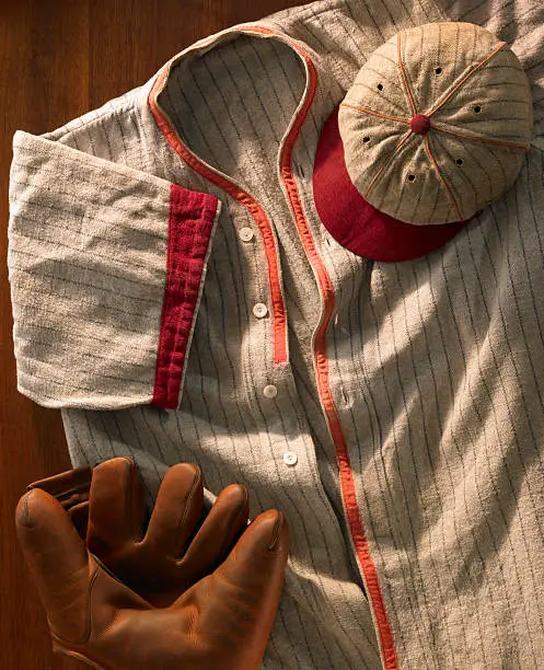 An vertical shot of antique pin-striped wool baseball uniform from the 20's with a matching cap and an old glove.