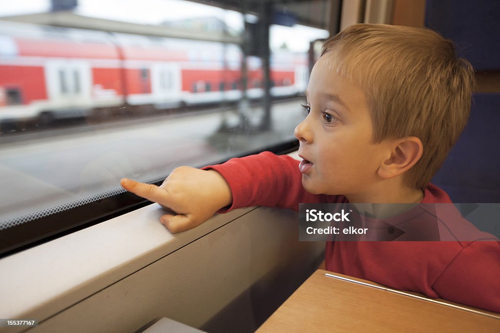 Cinq ans vieux petit garçon voyageant dans un train pointant à la fenêtre - Photo de Train libre de droits