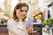 Surprised young woman use smartphone loses, bad news, fortune loss, fail outdoors in city street