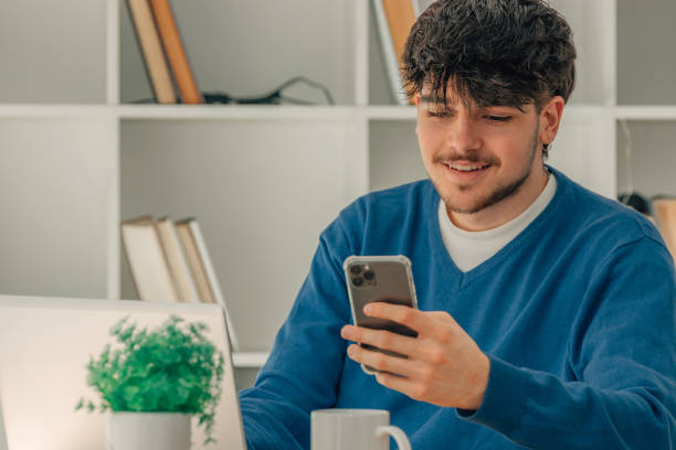istock young male student with mobile phone and laptop at desk 1553781069