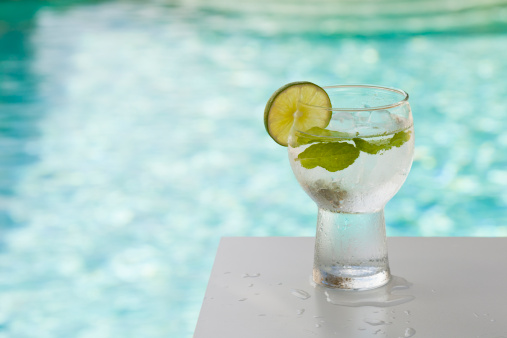 Glass of water with mint and lime on table by pool