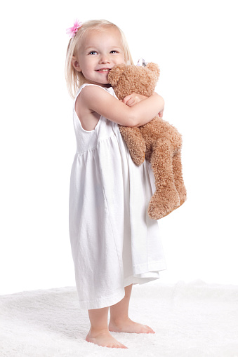 Little girl wearing white dress smiling on white background hugging a toy.