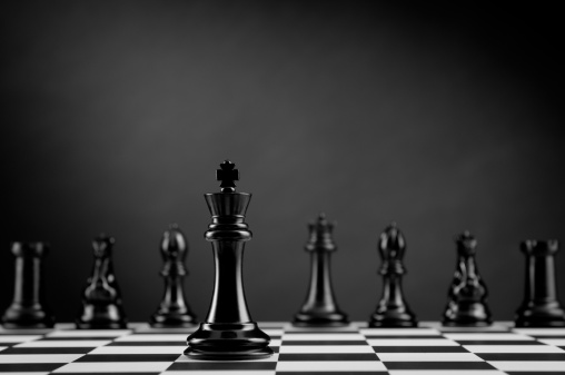 Leader and competition. Black Chess King on chess board against Chess Pieces on dark background.