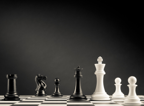 Black and white chess pieces on chess board against black background.