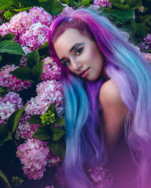 istock Young woman is surrounded by pink and violet hydrangea flowers. Beautiful model with a long colorful violet hair lying down on blooming hydrangeas flowers in garden 1553792856