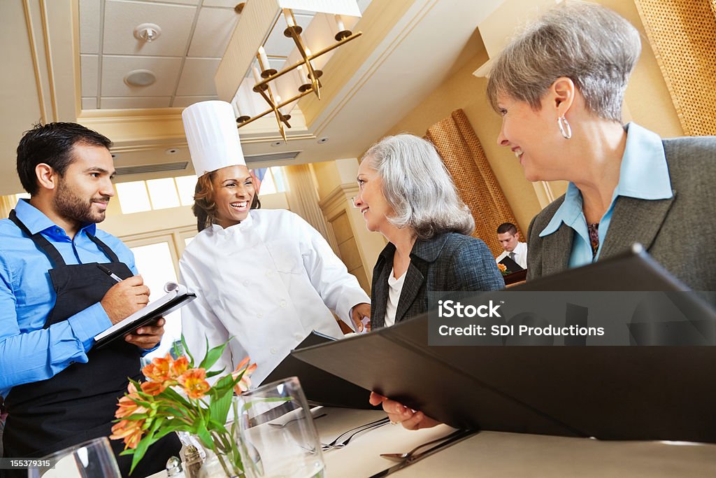 Lo Chef e camerieri ridere con i clienti e al contempo di rendere menu Suggerimenti - Foto stock royalty-free di Terza età