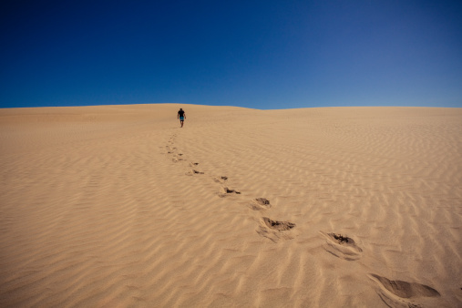 A man walking Hokianga's Great Sand Dunes in New Zealand. It looks like a naked desert.