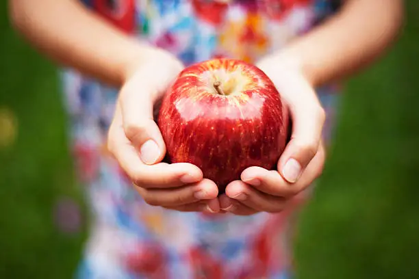 Photo of Depth of field apple held by a girl in colored dress outside