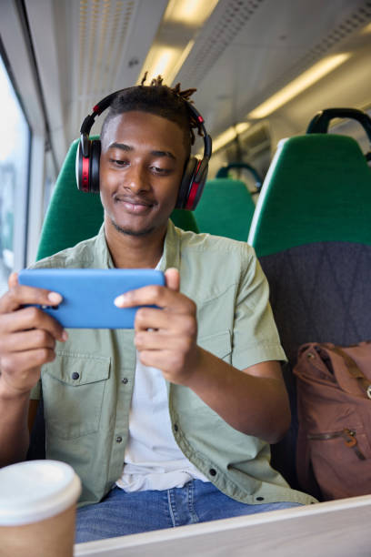 istock Young Man Commuting To Work Sitting  On Train Streaming And Watching Film Or Show On Mobile Phone 1553797782