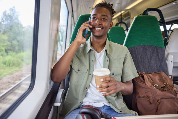 istock Young Man Commuting To Work On Train Sitting  On Train Talking On Mobile Phone With Takeaway Coffee 1553799939