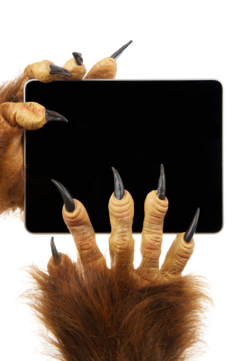 Scary monster Halloween hands with claws and werewolf fur hold digital tablet computer with blank screen against white background