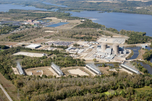 An aerial view of the Prairie Island Nuclear Power Plant, near Red Wing, Minnesota along the Mississippi River. The two pressurized water reactors produce approximately 1,100 megawatts. Shot from the open window of a small airplane. Four cooling tower units emit steam in the foreground. In the middle left is a secure area with multiple casks of nuclear waste. An Indian casino is in the background which makes for a good proximity  comparison between a nuclear plant and a populated area.