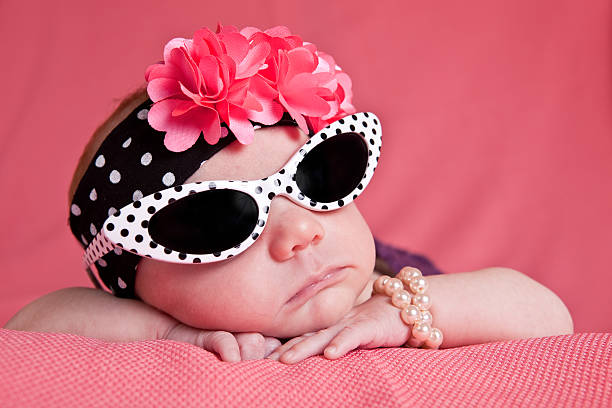 Newborn Girl in Sunglasses An adorable 1 month old baby girl dressed in sunglasses, headband and pearl bracelet. baby bracelet stock pictures, royalty-free photos & images