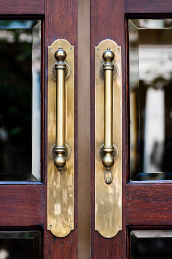 Closeup antique brass door handles on wooden door with glass windows, full frame vertical composition