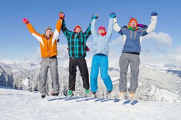 vier jungen menschen in winterkleidung jumping on snow - people group of people friendship salzburg stock-fotos und bilder
