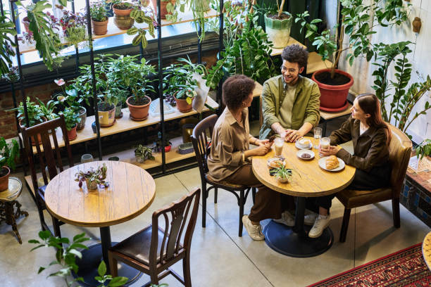 istock Happy young man and two intercultural women chatting by table in cafe 1553816903