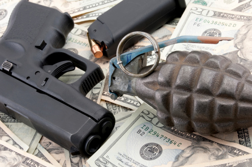 9mm handgun and pineapple grenade lying on hundreds of dollars in twenty-dollar bills laid out on a table.