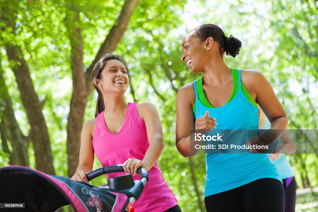 Felizes mulheres caminhando juntos no parque com carrinhos de bebê - Foto de stock de Fazer Cooper royalty-free