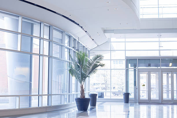 Modern office lobby with glass wall The lobby of a building in bright sunlight.  The walls are almost completely covered in windows, and the metal frames and door's are white.  The floor is reflective and there are three pots, one of them with a large plant in it. entrance sign photos stock pictures, royalty-free photos & images