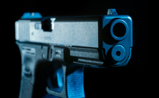 A close look at the barrel of a 9mm semi automatic pistol in hard studio light. Cold steel with a touch of blue.
