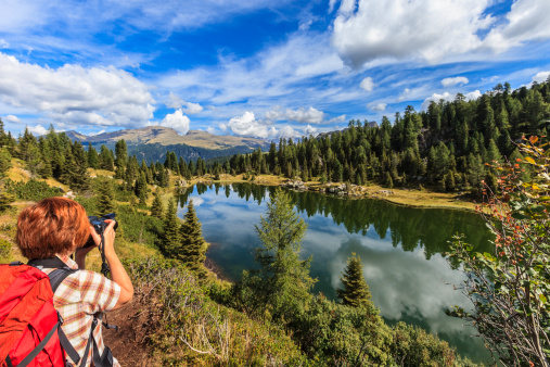 Photographer taking picture to the Colbricon lakes, two small lakes of glacial origin reachable from Passo Rolle after a walk in the Forest of Paneveggio. They are included in the Natural Park Paneveggio - Pale di San Martino, established in 1967, which includes the Trentino group of Dolomites of the Pale di San Martino, the eastern sector of the Lagorai massif and the spruce forest of Paneveggio. 