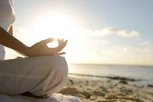 A woman is sitting at beach with yoga lotus position in the morning