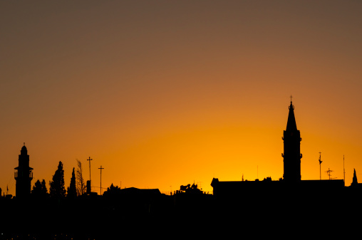 Sunset over the old city in Jerusalem. The minaret of a mosque is on the left; on the right is a church tower.